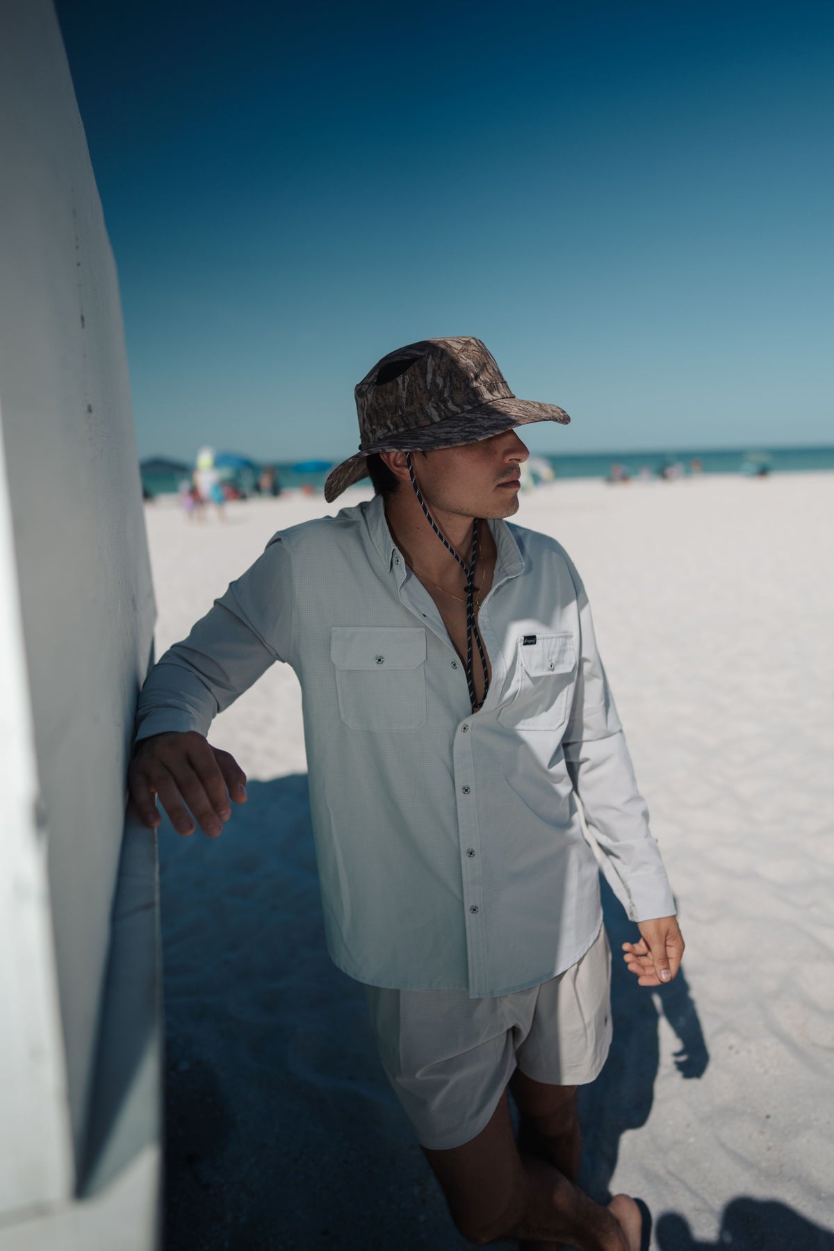 Person wearing a light gray shirt and camouflage hat on a sandy beach.