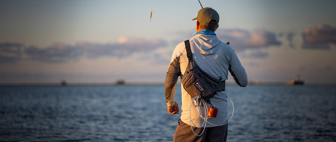 fly fisherman from the back in river with wade pack on his back and fly rod in hand