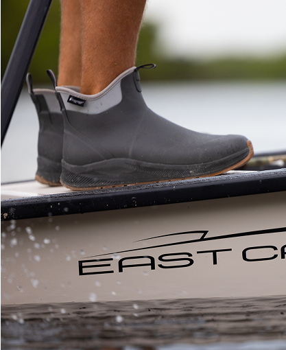 Closeup image of man wearing frogg toggs waterproof shoes, standing on a boat in the water.