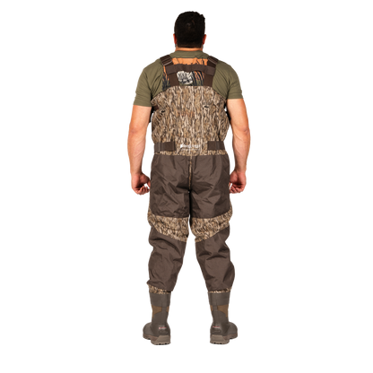 A man viewed from the back wearing a pair of brown and camouflage waders over an olive green shirt, standing against a solid white background.