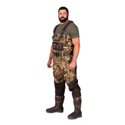 A man wearing camouflage duck waders over a green t-shirt and dark brown rubber boots, standing against a solid white background.