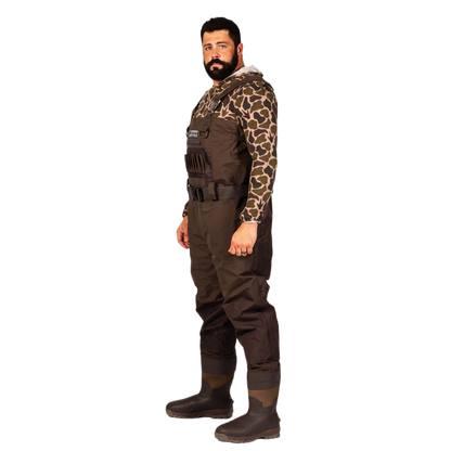 A man wearing a full-body brown wader with a camouflage long-sleeve shirt underneath and dark rubber boots, standing against a plain white background.
