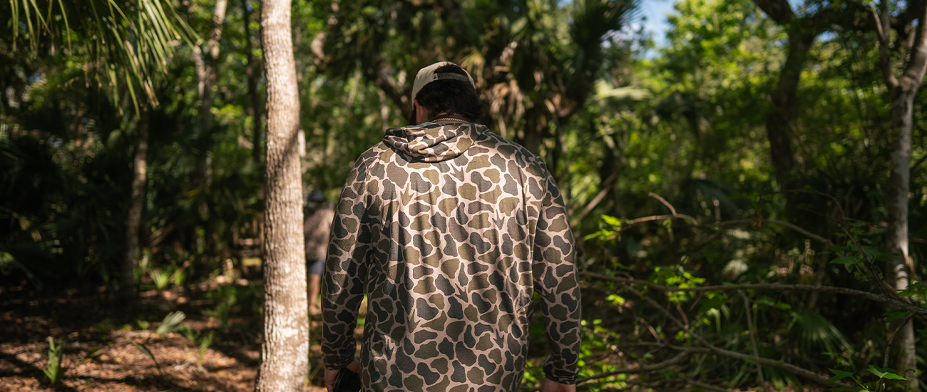 Guy in woods in long sleeved camo hoodie