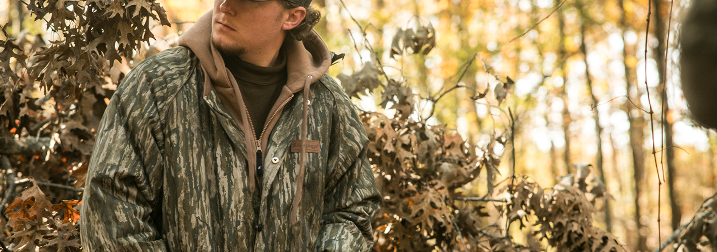 Person wearing a camouflage jacket in a forest setting