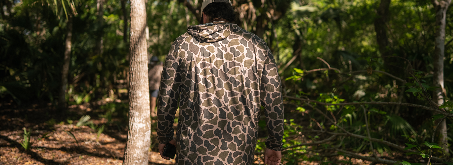 Person wearing a camouflage outfit walking through a forest