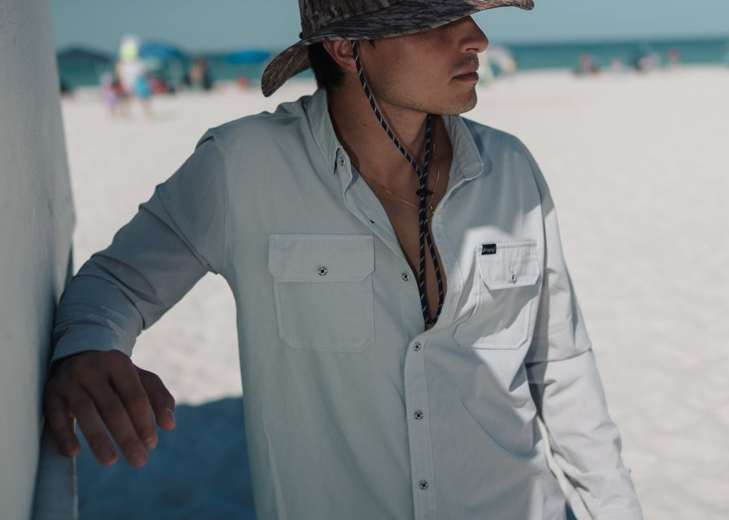 Person wearing a light blue shirt and camouflage hat on a sandy beach.