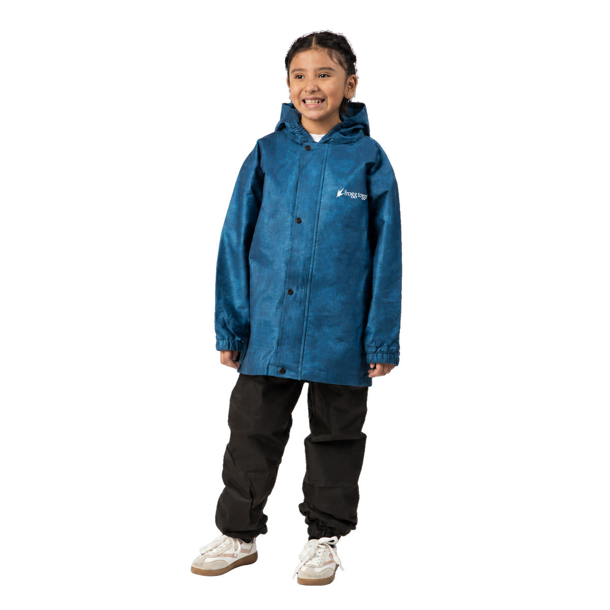 A young girl wearing a blue hooded Frogg Toggs raincoat with black pants and white sneakers, standing against a solid white background.