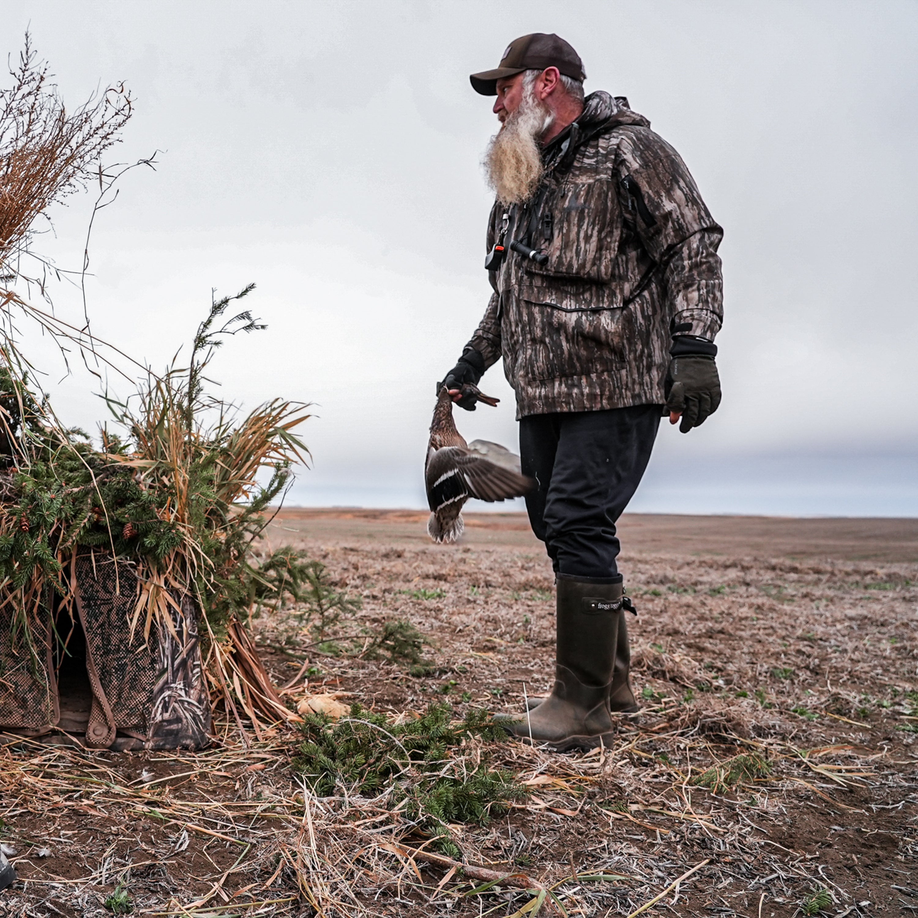 Man in camouflage hunting gear holding a duck in a field