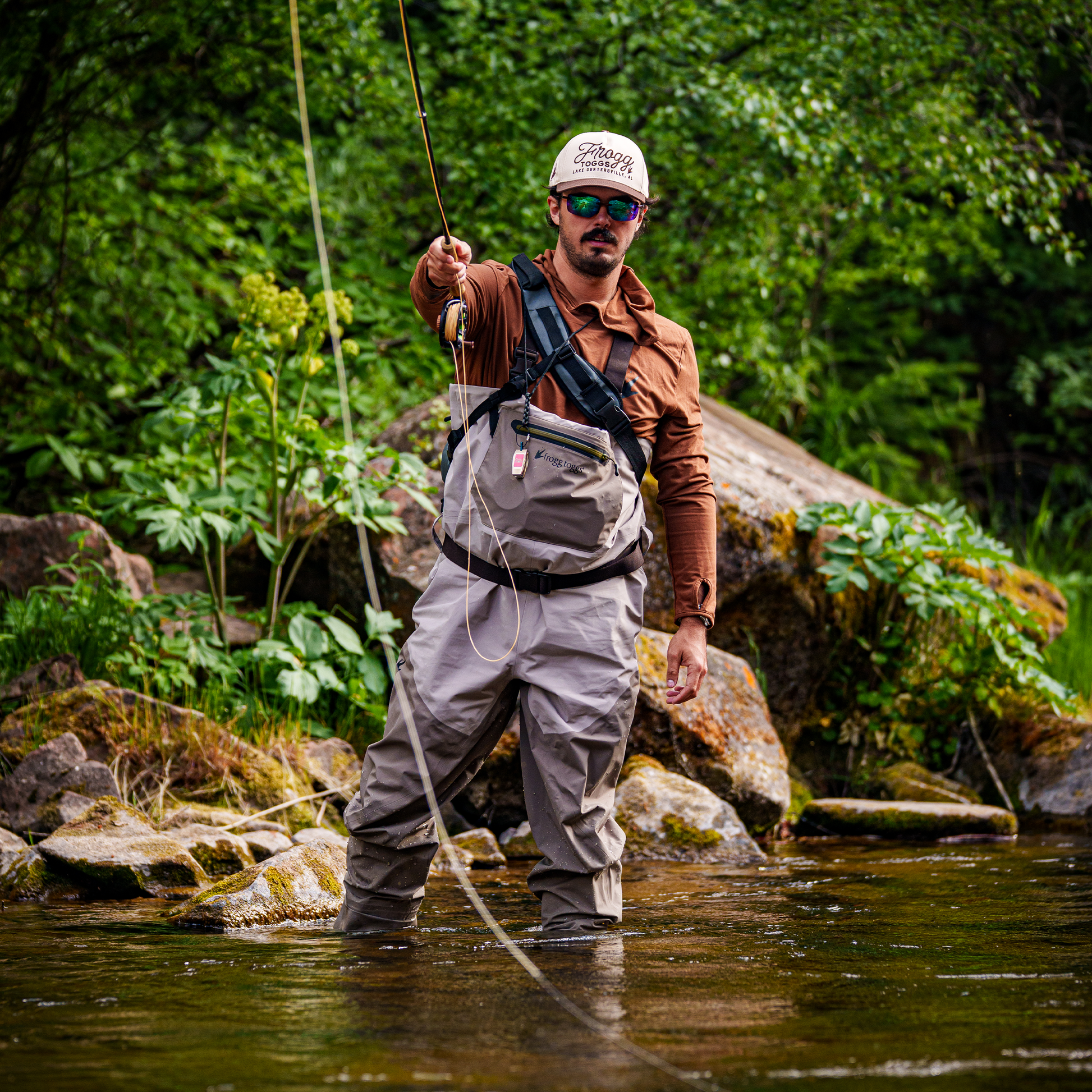 Man fly fishing in a stream surrounded by greenery