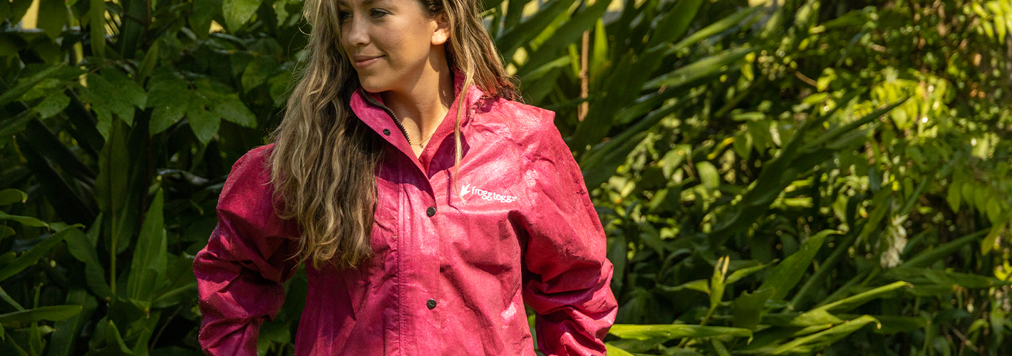 Woman wearing a pink raincoat standing in a lush green outdoor setting