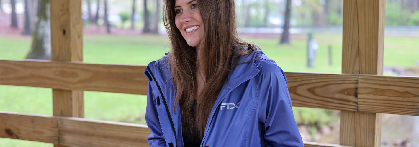 Woman wearing a pink raincoat standing in a lush green outdoor setting